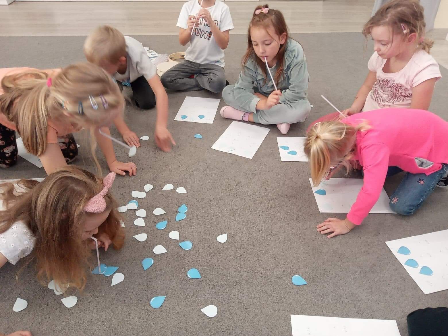 dzieci słomkami przenoszą krople deszczu z papieru
