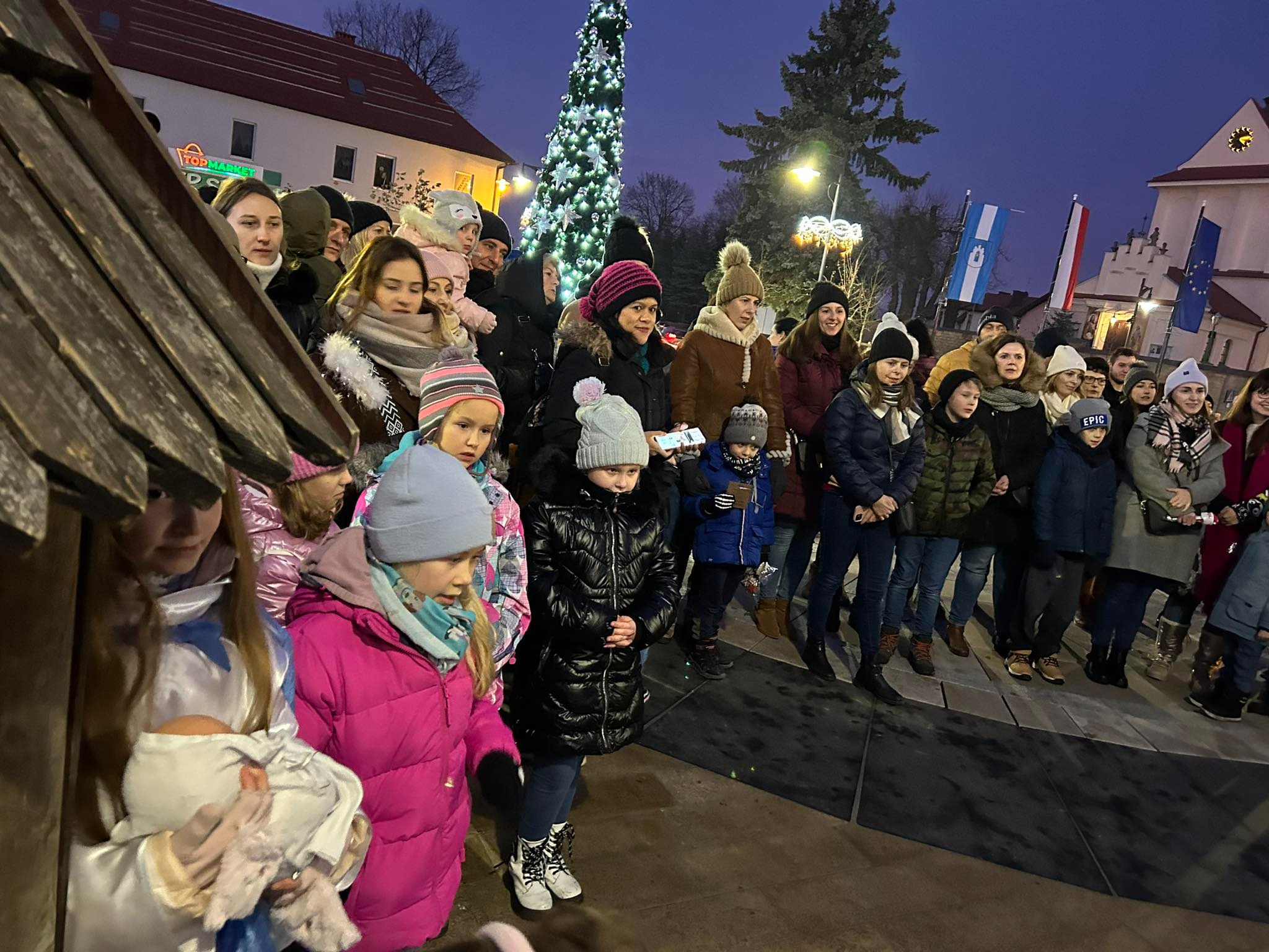 rodzice z dziećmi kolędują przy szopce